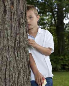 Child with Social Anxiety Disorder hiding behind tree at park