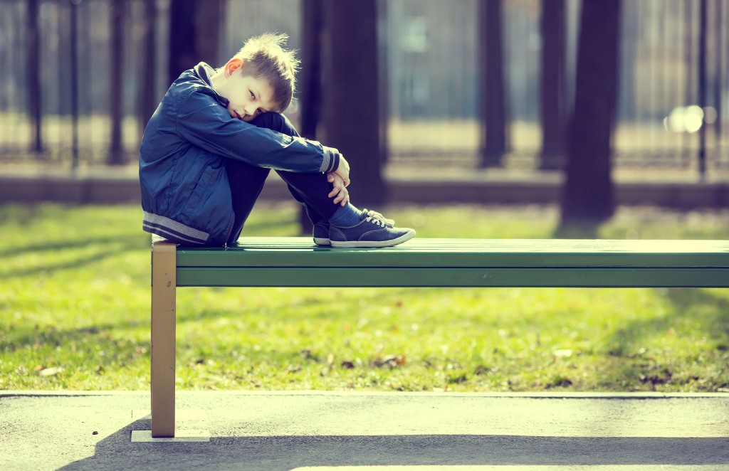 little boy alone and sad curled up on school bench.