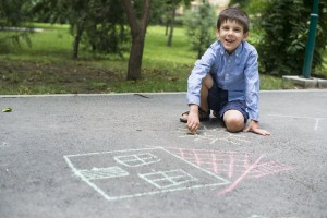 smiling boy playing with chalk on sidewalk