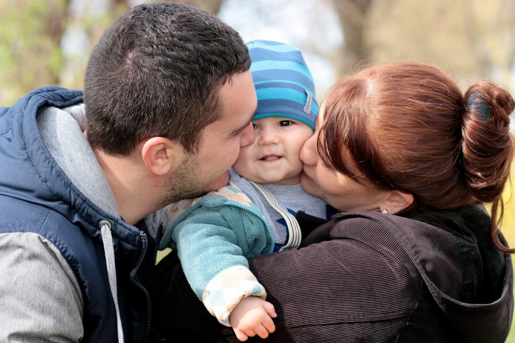 Mother and Father kissing their infant baby on the cheek.