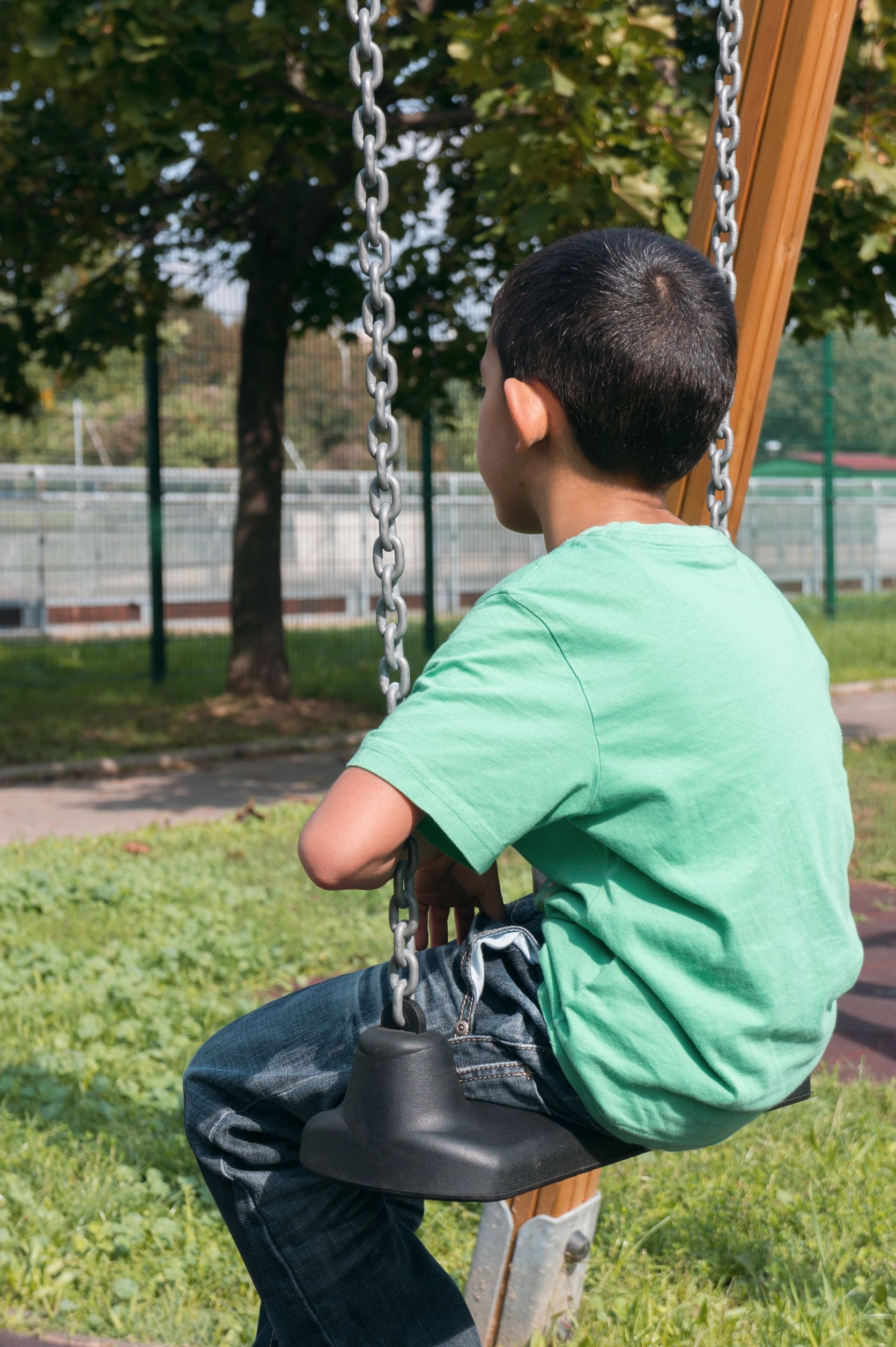 young boy with social Anxiety sitting on park swing alone 
