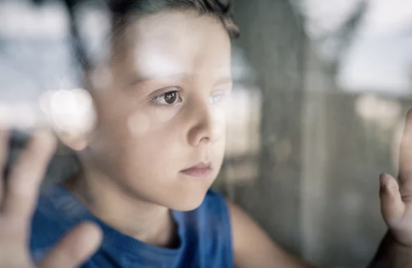 young boy with social anxiety looking out glass window