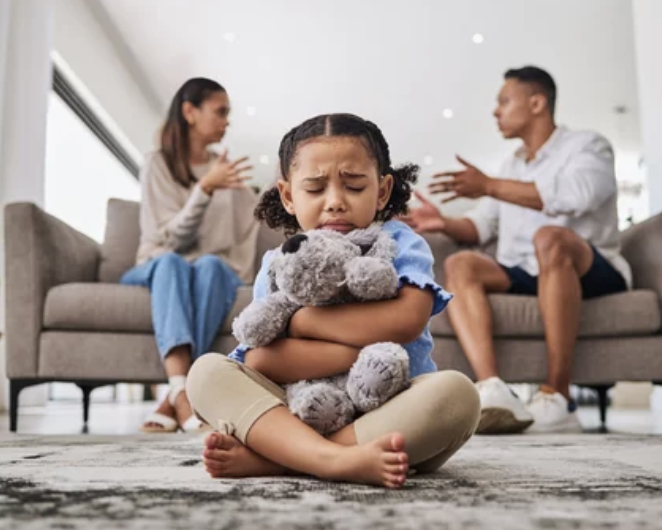young girl with ptsd crying holding teddy bear while parents argue behind her