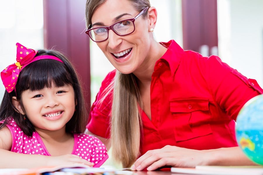 ABA therapist/Psychologist and child smiling while reading looking up at camera.