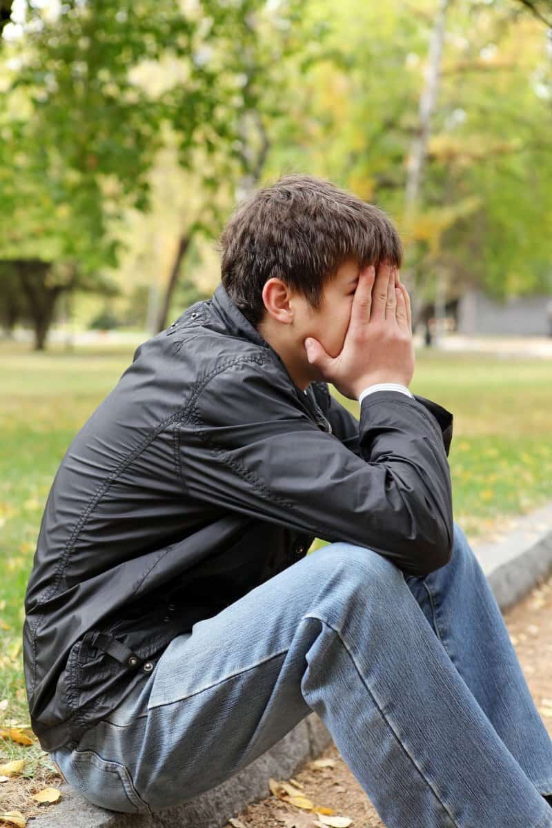 sad teen holding his face in park