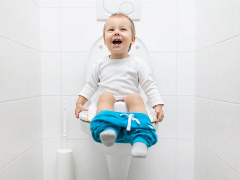 Toddler potty training sitting on toilet smiling.