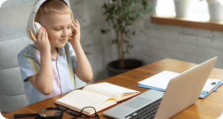 Little boy with headphones at home looking at laptop working on homework.