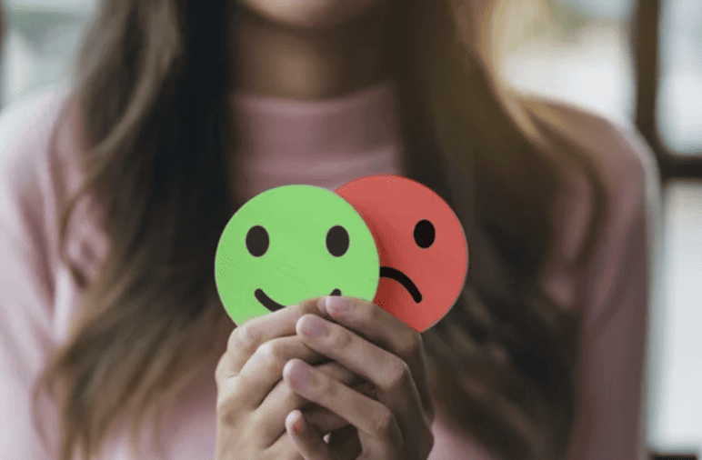 Girl with Anxiety holding up cut outs of happy face and sad face