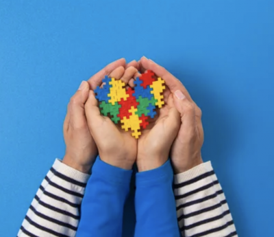 close up of Parent hands holding child with autism holding heart shaped puzzle pieces.