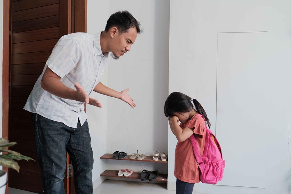 Parenting with hands spread asking why his child is refusing to go to school. Child has her hands covering her face.